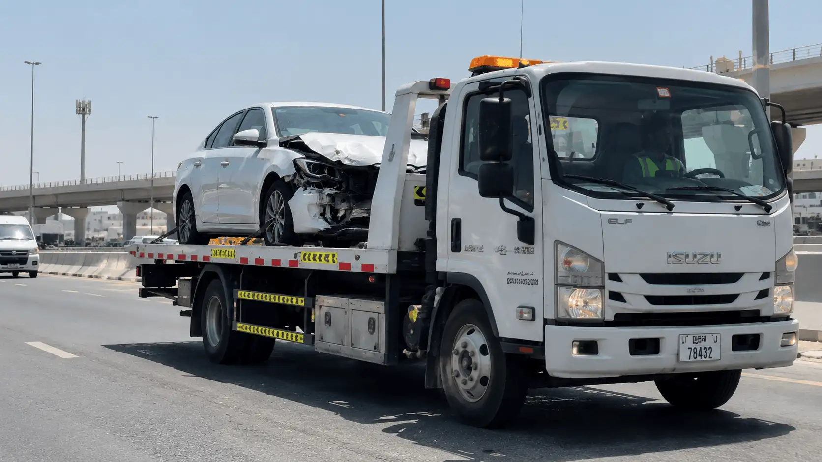 White Isuzu recovery truck towing a damaged car on a UAE road